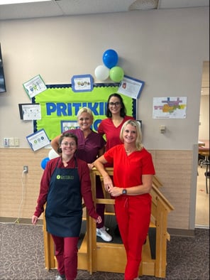 The four person staff at Clinton Regional Hospital cardiac rehab. All are standing in front of a bulletin board decorated with balloons and Pritikin colors. They are standing on and around a little wooden step frame.