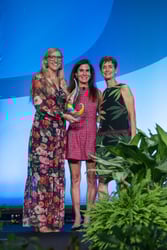 Cindy Berner stands with two women from ACLM as she accepts Nathan Pritikin's Lifetime Achievement Award, a colorful glass award shaped like a drop with a swirl.