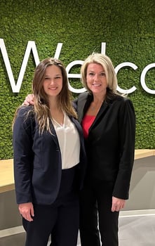 Tara and Kathryn, two women in suits stand next to each other smiling for the camera.