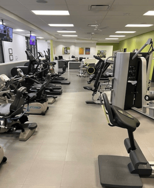 Fitness equipment arranged in a room shaped like a long rectangle. One wall is pea green and the floors are two shades of grey.