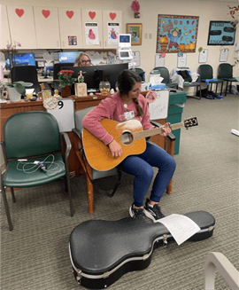 Leah McClure sits with her guitar singing and playing for cardiac rehab patients
