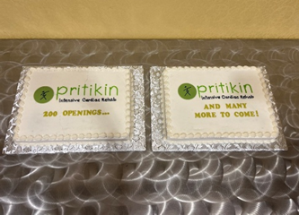 two white cakes with the Pritikin logo. Between the two cakes, written in green icing is "200 openings...and many more to come!"