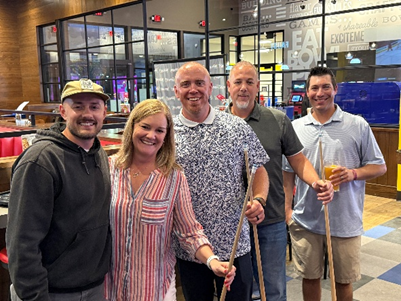 5 smiling Pritikin employees pause their billiards game to pose together for a picture.