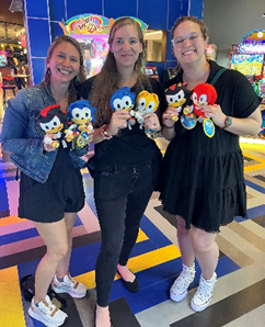 Three Pritikin employees stand together holding stuffed animals they won in a claw machine game.