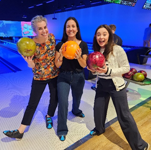 Three women, each holding a bowling ball, pose for a team photo.