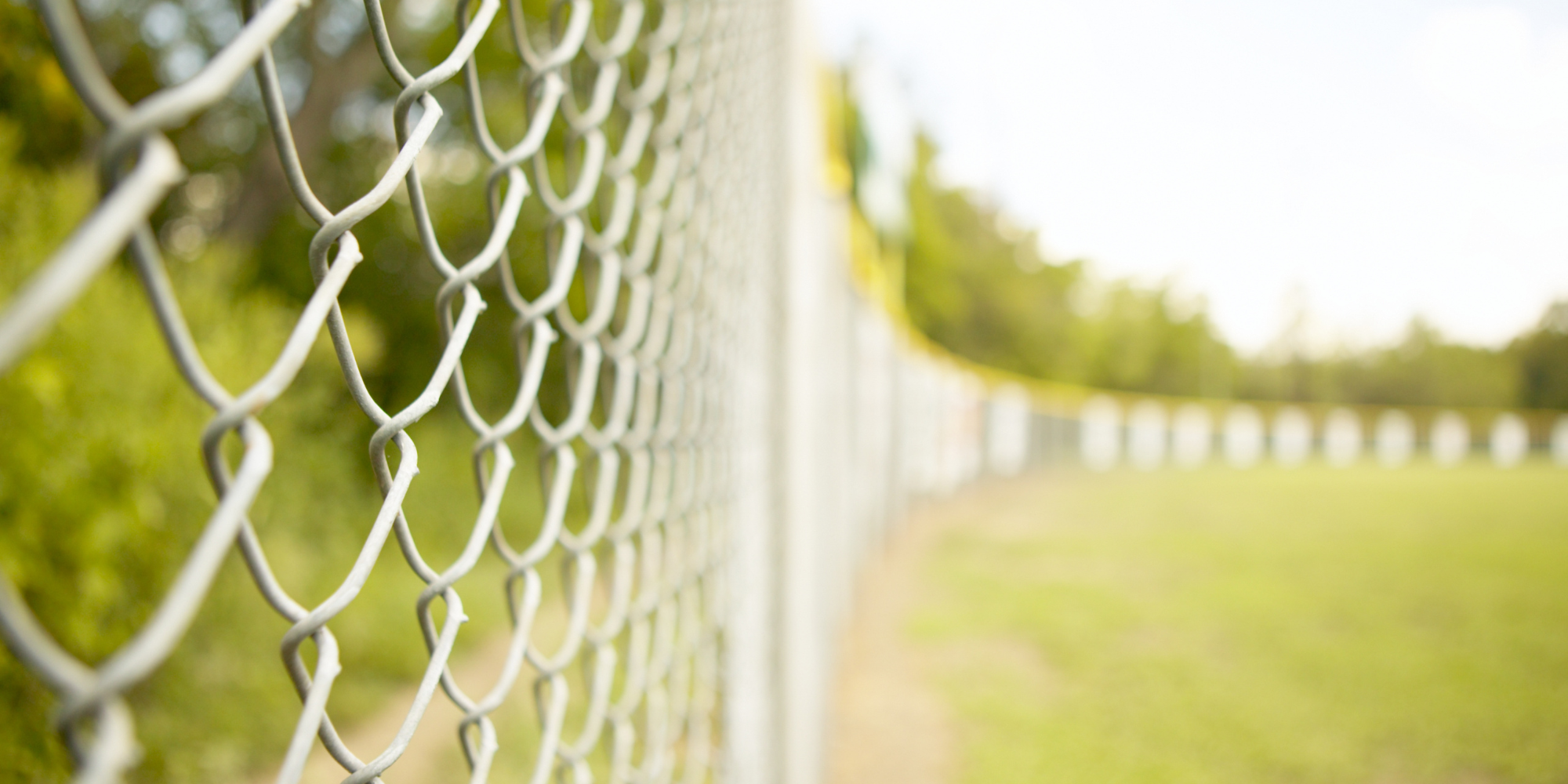 Silver chain link fence around a green park/baseball field