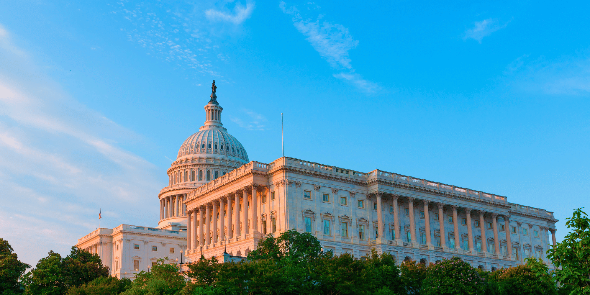 Exterior photo of the US Capital building viewed from the right side of the building. The sky is bright blue and the sun is shining.