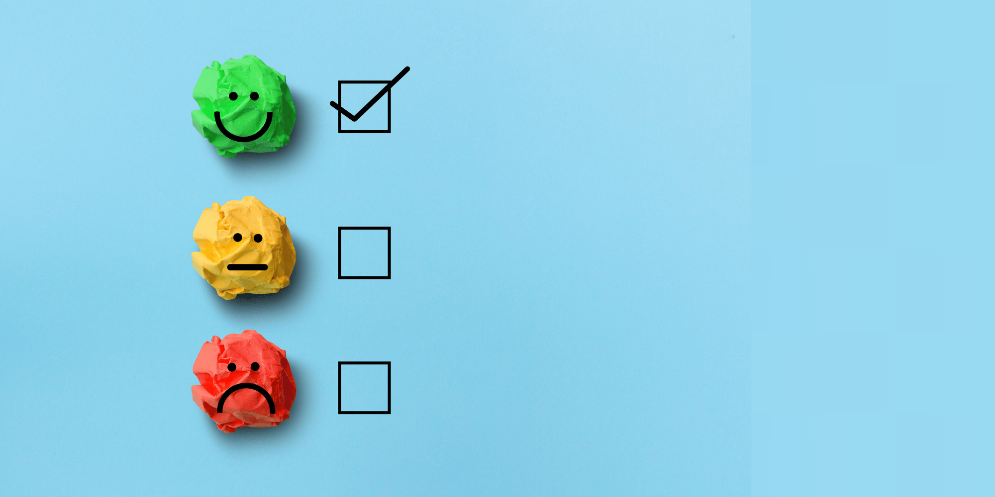 Three crumpled balls of paper lined up one above the other. They are the color of a traffic light with green at the top, yellow in the center, and red at the end. Each has a little face over it green is happy, yellow is neutral, and red is sad. Next to each is a little check box. The only box with a check in it is the one next to the green smiley face.