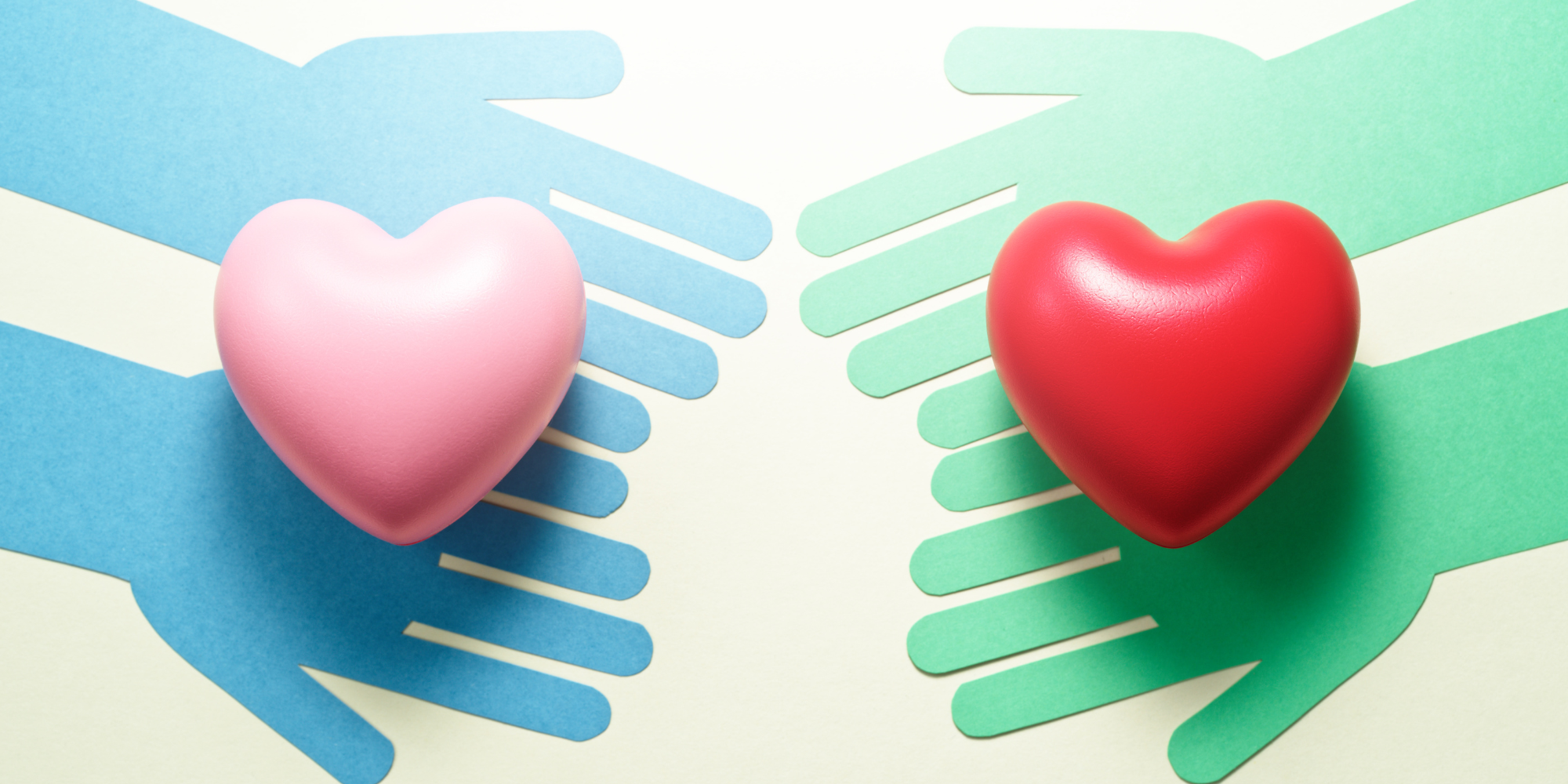 Two pairs of paper cut-out hands (the left pair is blue and the pair on the right is green) extend towards each other from opposite sides of the page. Each is holding a heart..