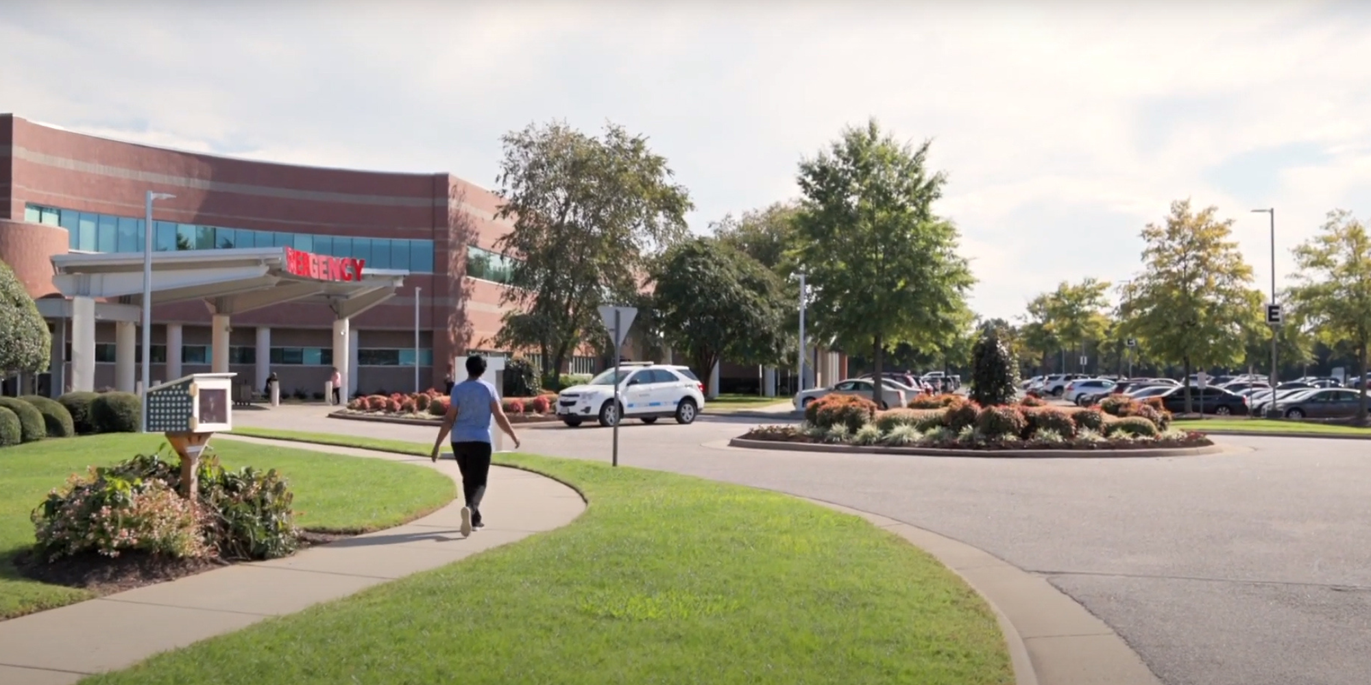 Woman walks on a sidewick along a manicured path into the Sentara CarePlex Intensive Cardiac Rehab building. 
