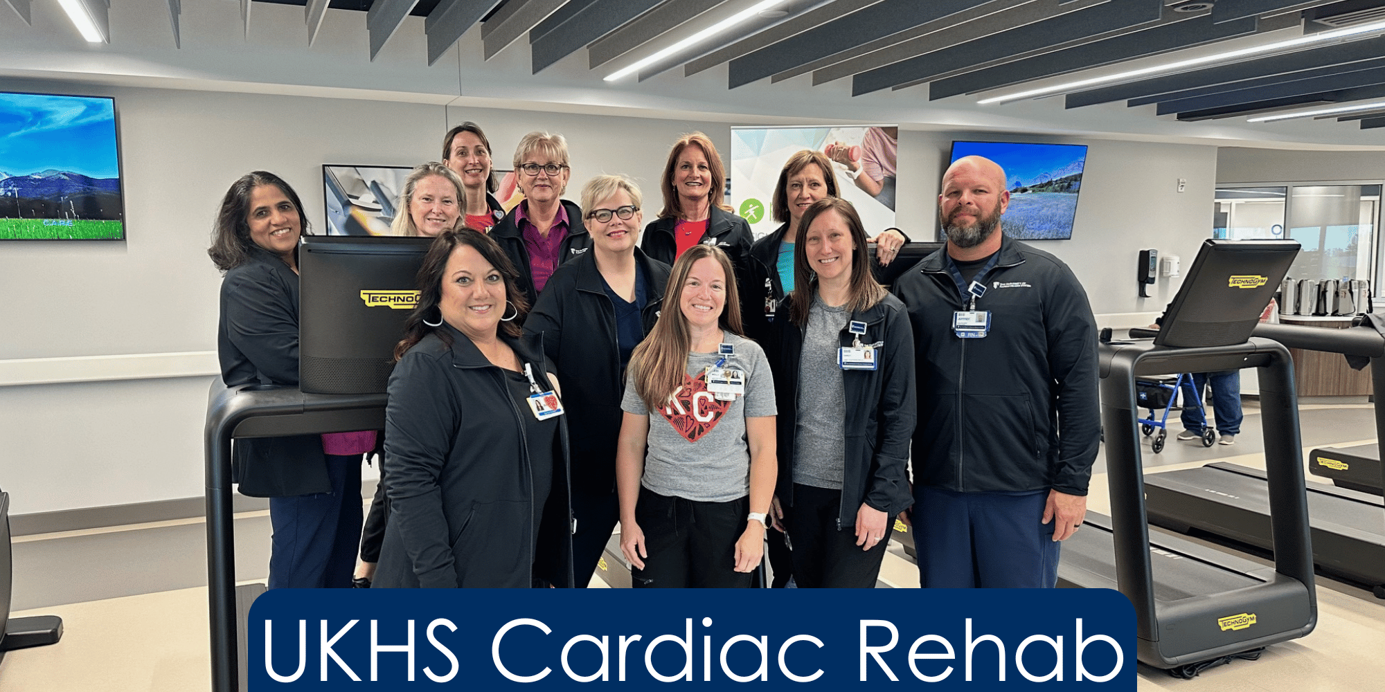Eleven Cardiac Rehab professionals standing in the exercise area of their facility. All are smiling at the camera and wearing scrubs. At the bottom of the picture, reads "UKHS Cardiac Rehab"