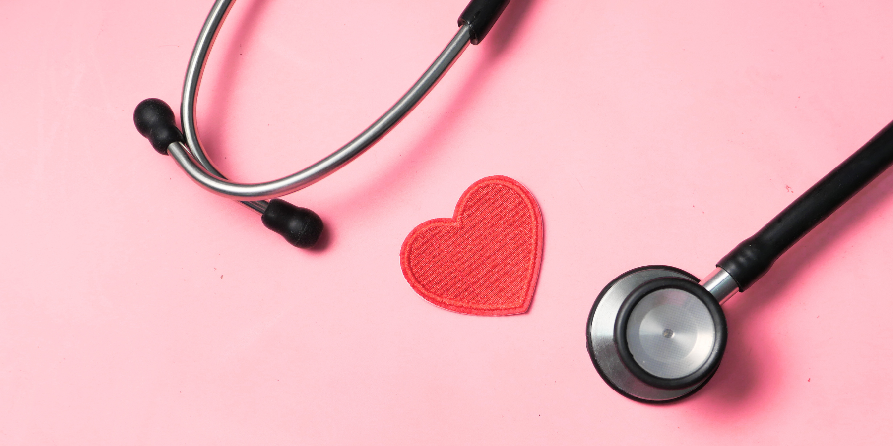 A stethoscope against a pink background with a cut-out red heart 